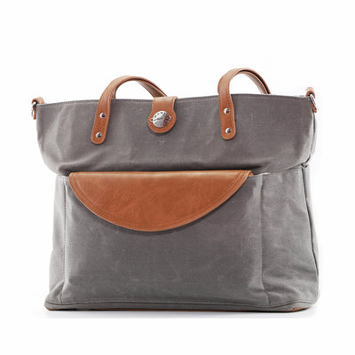 Grey canvas tote bag with brown vegan leather accents and clutch tucked in front pocket, shown on white background.
