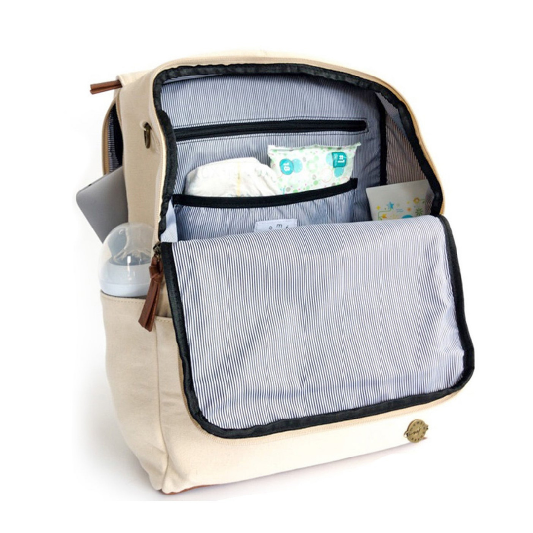 A front-facing 3/4 view of a stone colored waxed canvas backpack diaper bag with front flap zipped open showing pockets inside, a baby bottle in side pocket, and a laptop in separate back compartment. Wipe-clean lining is a thin black and white stripe pattern with black accents. Image shown on a white background.
