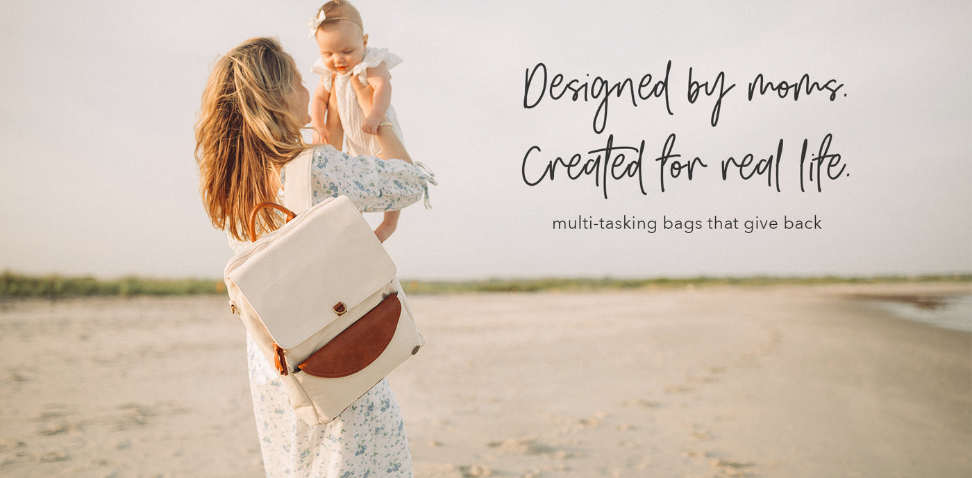 A mom standing on the beach holding her baby in the air wearing a stone colored backpack with the headline "Designed by moms. Created for real life."