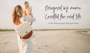 A mom standing on the beach holding her baby in the air wearing a stone colored backpack with the headline "Designed by moms. Created for real life."