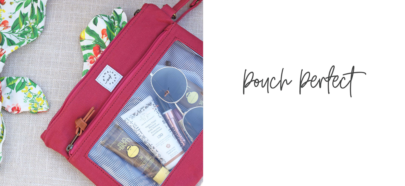 A berry-colored canvas Pack-it-Up Pouch filled with some lotions, sunglasses and other small essentials, laying on a mat with a bathing suit coming out of the pack pocket. 