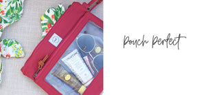 A berry-colored canvas Pack-it-Up Pouch filled with some lotions, sunglasses and other small essentials, laying on a mat with a bathing suit coming out of the pack pocket. 