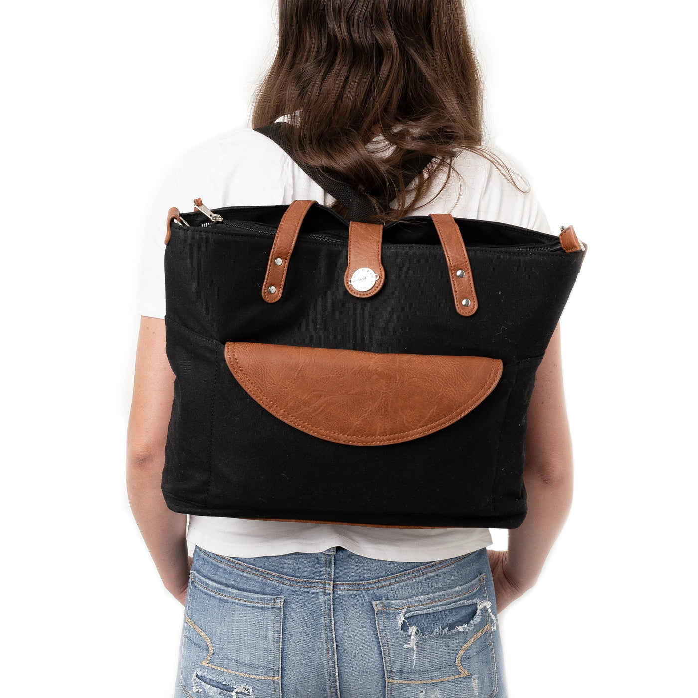 Mom in jeans and a white t-shirt standing backwards wearing a black waxed canvas backpack with brown vegan leather accents, all on a white background.