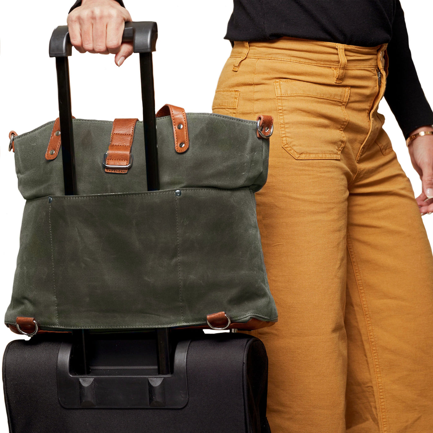 Forest green waxed canvas tote mounted on luggage handle of black rolling bag using sleeve pocket, with mom pulling.