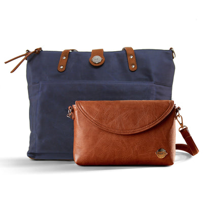 Navy blue waxed canvas tote with brown vegan leather accents and brown vegan leather diaper clutch, all on a white background.
