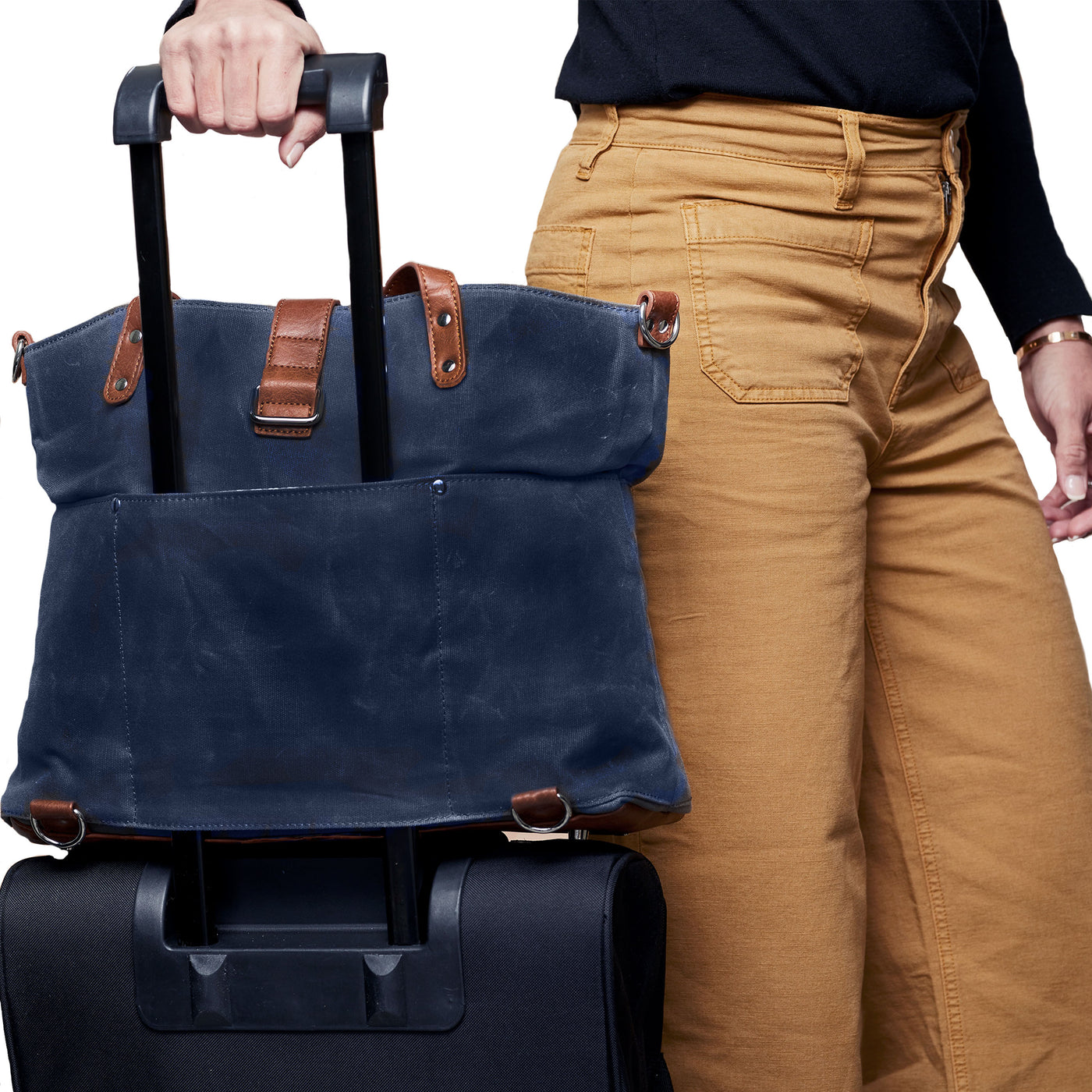 Woman walking with navy blue tote attached over handle of rolling suitcase via trolley sleeve on backside of tote.