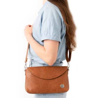 Woman in blue blouse turned sideways wearing a caramel brown vegan leather crossbody bag.