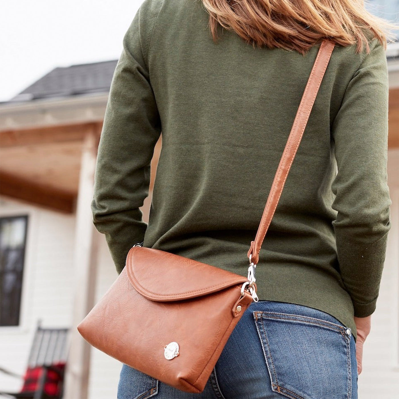 Brown vegan leather Diaper Clutch with zipper closure includes a crossbody strap and changing pad worn crossbody on woman.