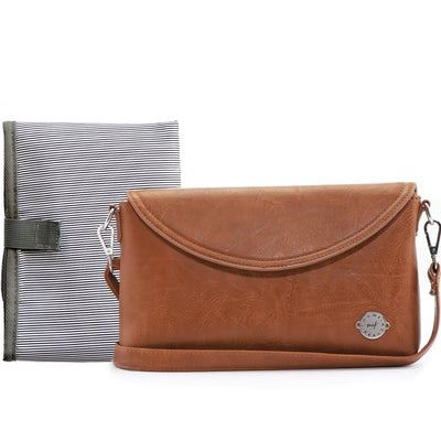 Caramel brown vegan leather clutch with crossbody strap on white tabletop, with folded B&W striped changing mat behind it. 