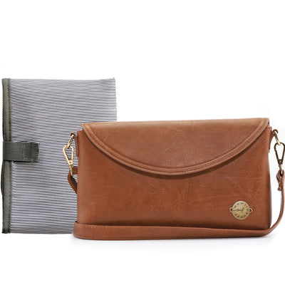 A caramel brown vegan leather crossbody clutch shown with a folded black & white striped changing mat on white background.