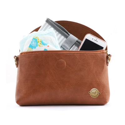 A caramel brown vegan leather clutch bag, unzipped with flap open and showing cell phone, diaper, wipes case and changing mat inside, all on a white background.