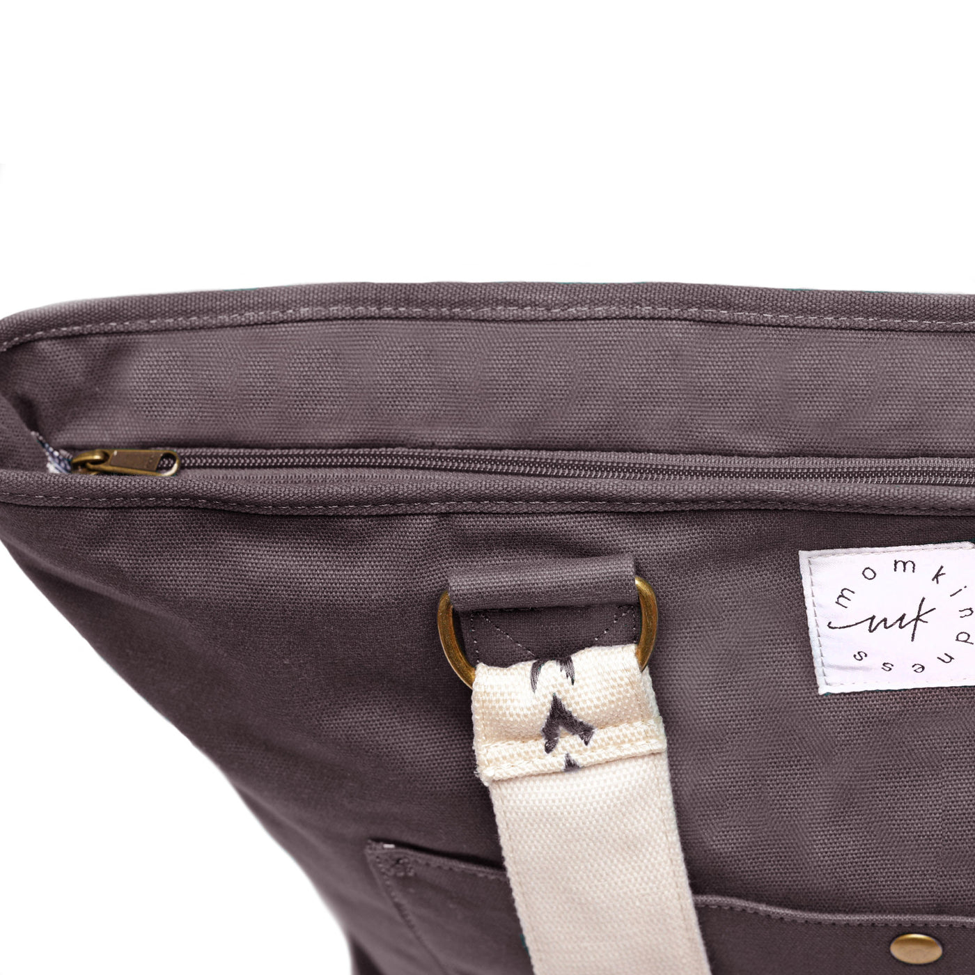 A close-up of the zipper-top panel of an extra-roomy canvas weekender tote in a graphite color with ivory embroidered shoulder straps with an arrow pattern, shown on a white background.