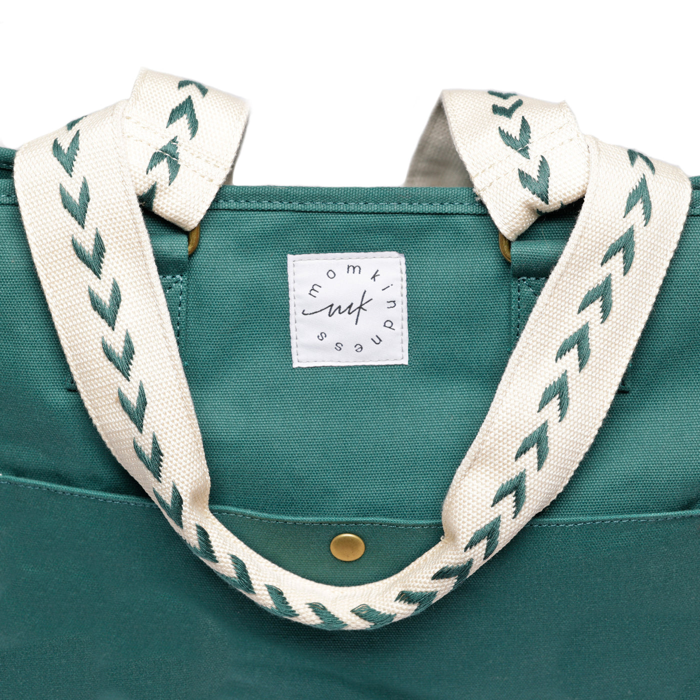 A close-up of the arrow pattern embroidered beige shoulder straps on a Juniper green colored canvas tote and showing the Momkindness logo patch.