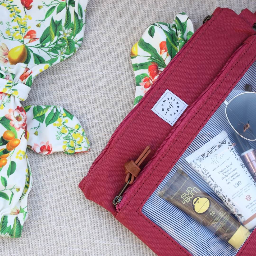 Berry Pouch with wet pocket in back with bathing suit coming out and front clear pocket window showing sunscreen and sunglasses.