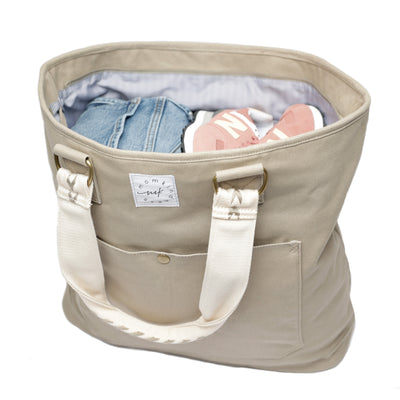 A large capacity canvas tan-colored tote shown at 3/4 angle and loaded with clothes, sneakers, etc.