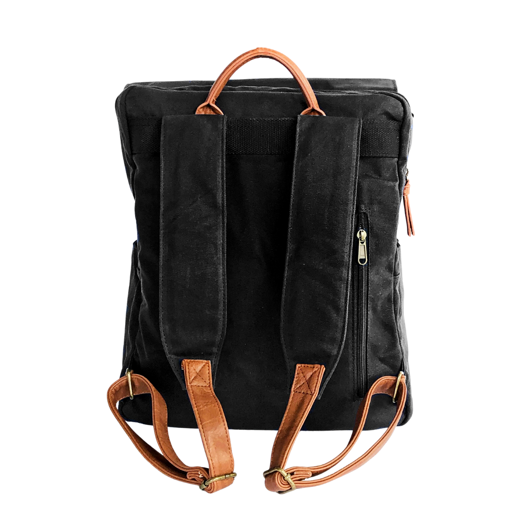 Backside view of black waxed canvas backpack that shows extra comfort-padded canvas straps with brown vegan leather adjustable strap ends with bronze buckles and brown vegan leather carry handle on top. Image shown on a white background.