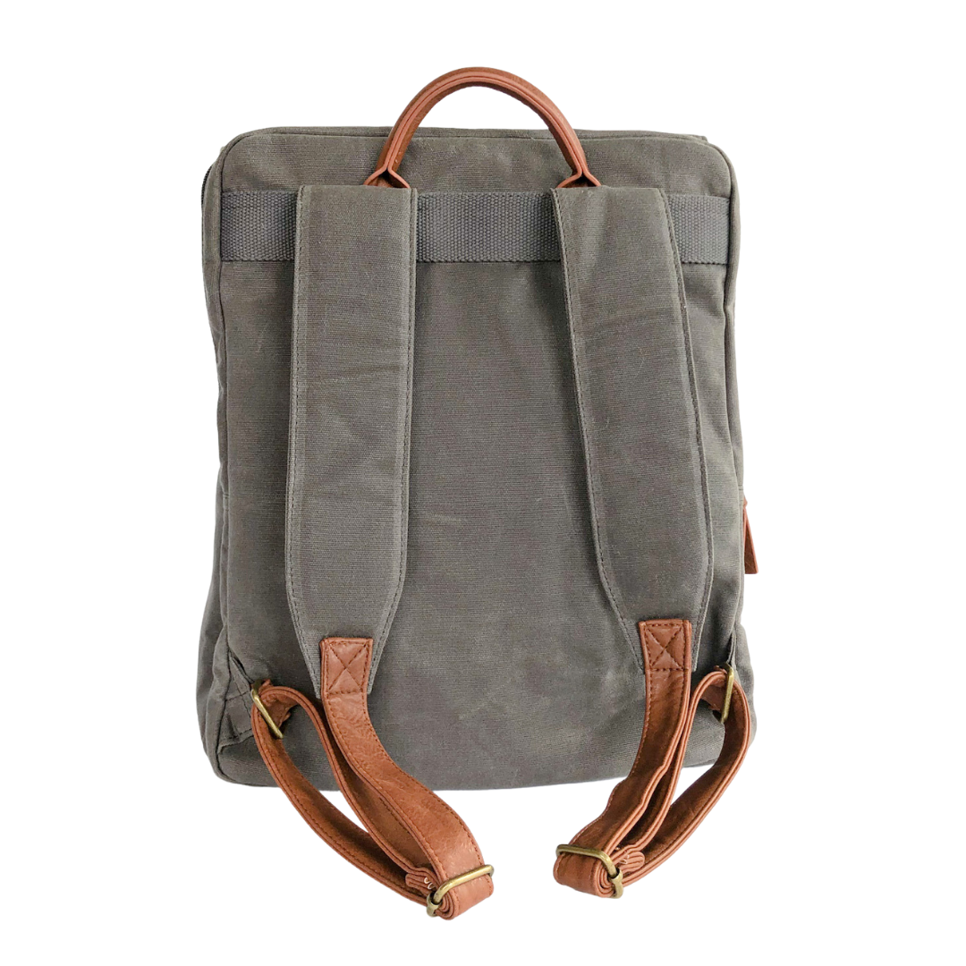 Backside view of grey waxed canvas backpack that shows extra comfort-padded canvas straps with brown vegan leather adjustable strap ends with bronze buckles and brown vegan leather carry handle on top. Image shown on white background.