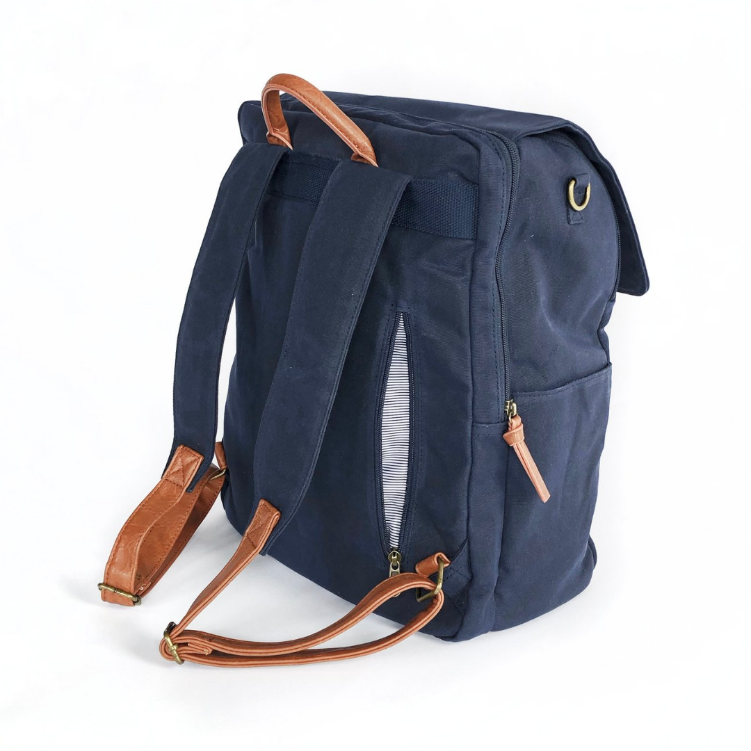 A back-facing 3/4 view of navy waxed canvas backpack that shows zip-close back pocket in open position that conveniently stores items that need to be easily accessible. Side water bottle pocket and separate padded laptop pocket that has a zipper closure also shown. Image shown on white background.