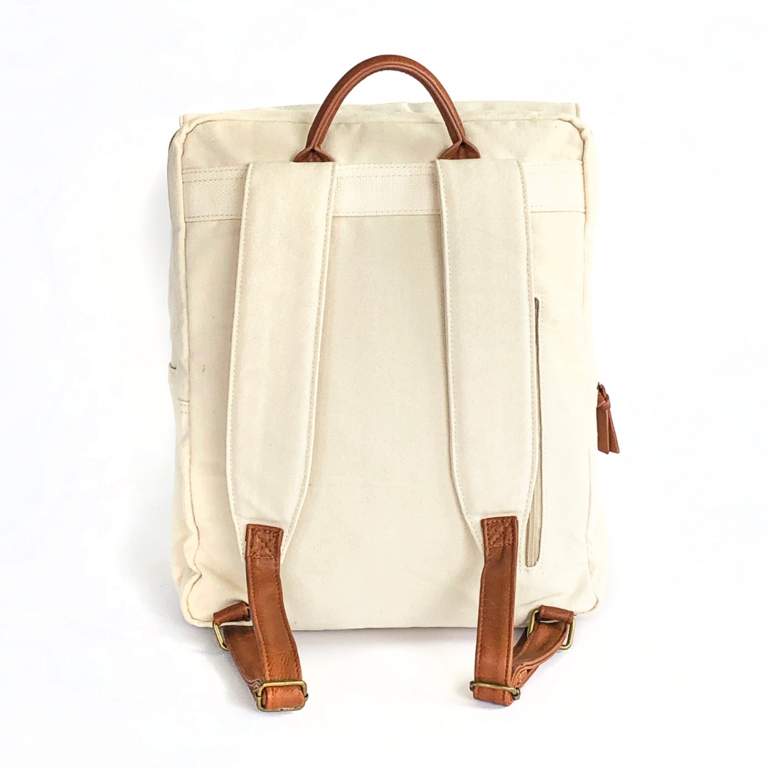 Backside view of stone colored canvas backpack that shows extra comfort-padded canvas straps with brown vegan leather adjustable strap ends with bronze buckles and brown vegan leather carry handle on top. Image shown on a white background.