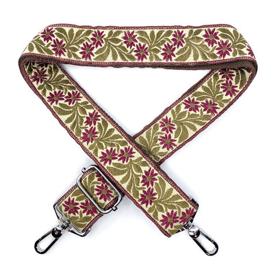 A close-up on white background of an embroidered, adjustable length bag strap, 1.5 inches wide with burgundy, green and gold floral pattern and silver clasp.